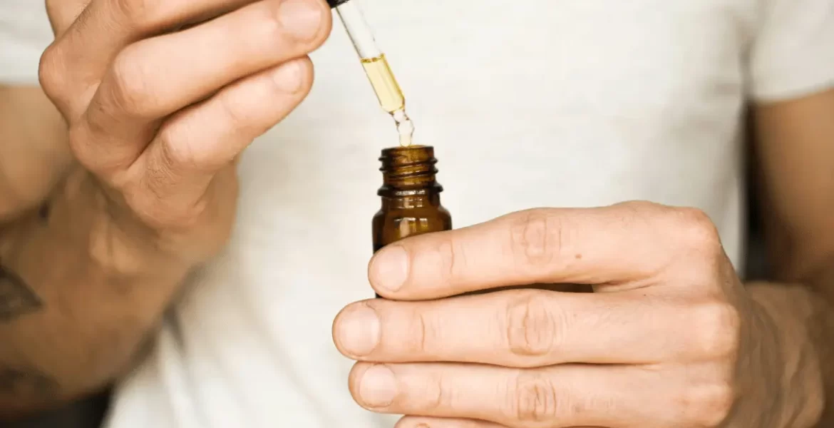A man holding a CBD oil bottle with a dropper. Read more in the article 'How to Measure CBD Oil Tincture Strength?'.