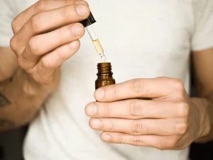A man holding a CBD oil bottle with a dropper. Read more in the article 'How to Measure CBD Oil Tincture Strength?'.